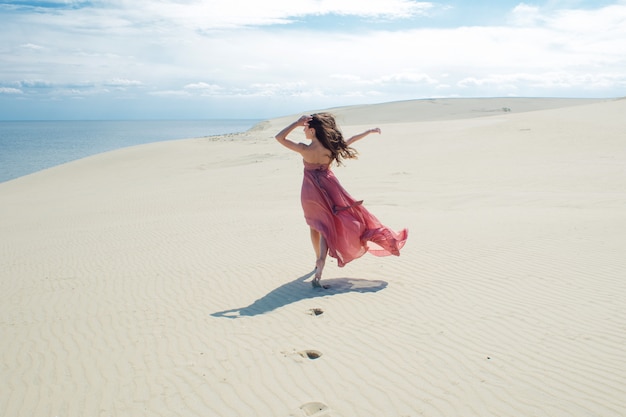 Een jonge mooie vrouw in een roze jurk loopt op de duinen