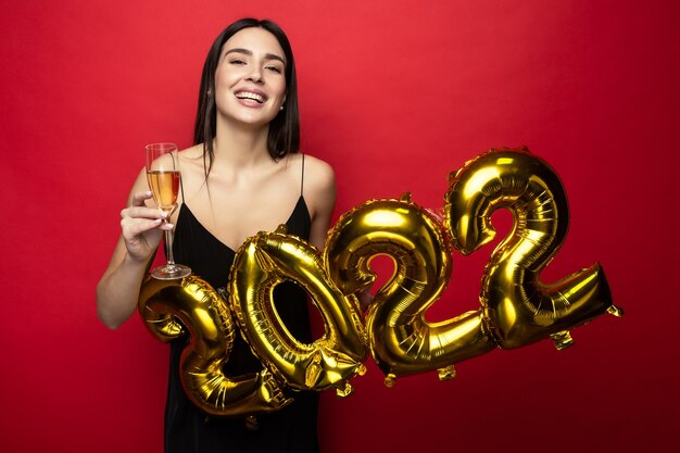 Een jonge mooie vrouw in een zwarte jurk houdt de nummers 2022 vast en een glas champagne