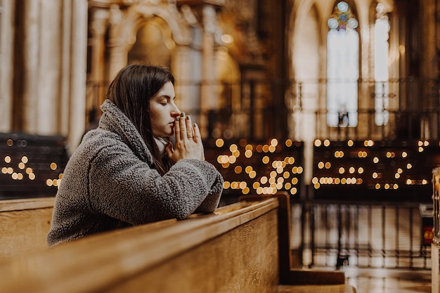 Een jonge mooie vrouw kwam naar de tempel om tot God te bidden De parochiaan van de kerk zit op een bank met haar handen gevouwen voor gebed en bidt hartelijk