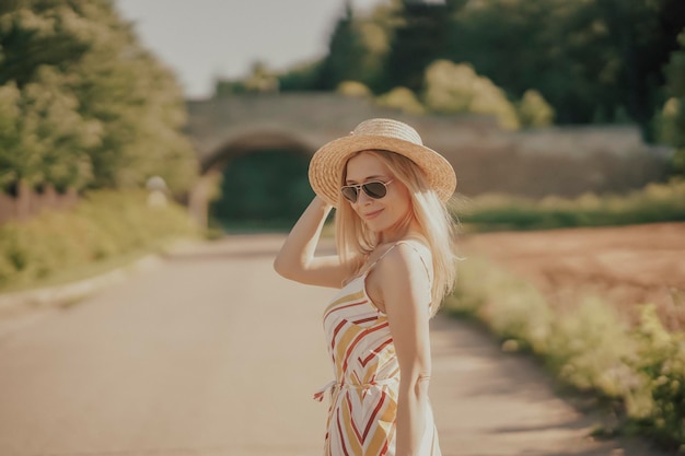 Een jonge mooie vrouw met een strohoed die langs de weg loopt