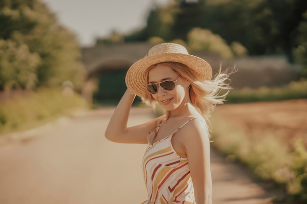 Een jonge mooie vrouw met een strohoed die langs de weg loopt