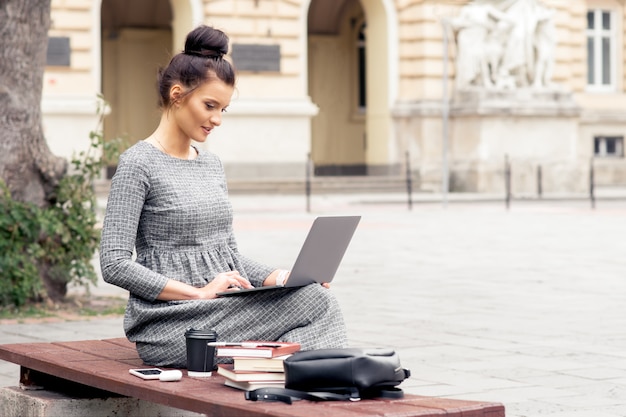 Een jonge mooie vrouw werkt op laptopcomputer in de buurt van de bouw van de universiteit.