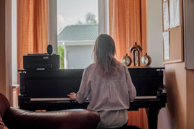 Een jonge mooie vrouw zit met haar rug naar ons toe en speelt piano, muzieklessen bij jonge mensen