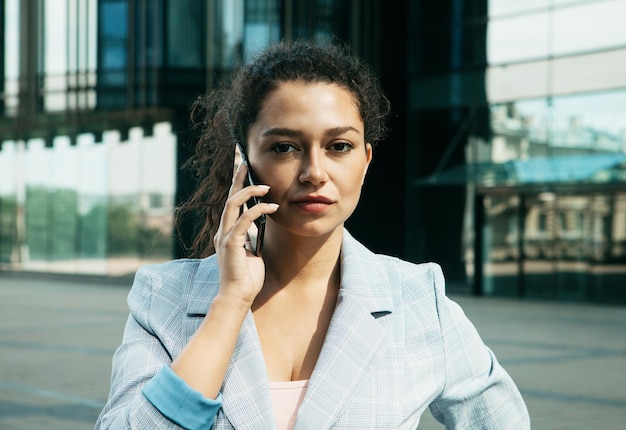 Een jonge mulatvrouw tegen de achtergrond van een zakencentrum houdt een mobiele telefoon vast en praat