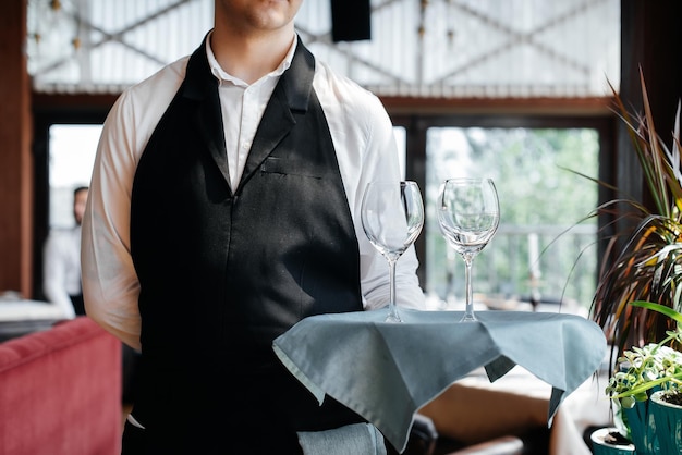 Een jonge ober staat met wijnglazen in een stijlvol modern restaurant Service aan tafel in het restaurant Haute cuisine service en onderhoud Close-up