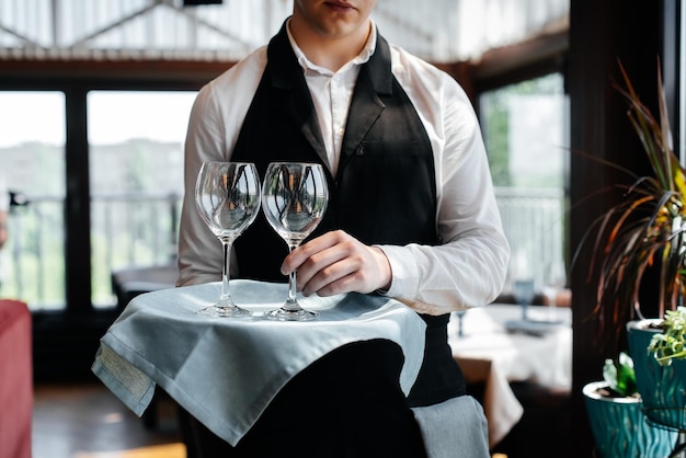 Een jonge ober staat met wijnglazen in een stijlvol modern restaurant Service aan tafel in het restaurant Haute cuisine service en onderhoud Close-up