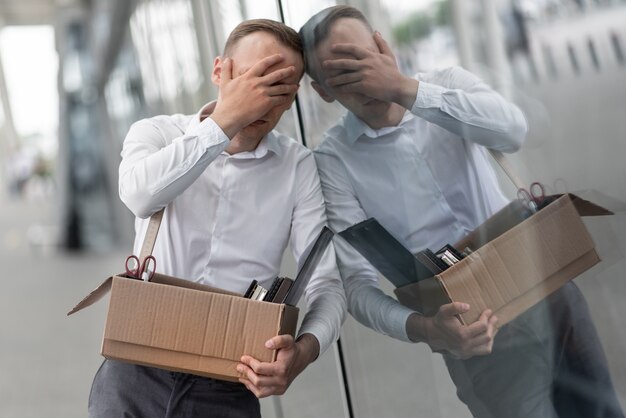 Een jonge ontslagen kantoormedewerker beet op het glas van een modern kantoorgebouw.