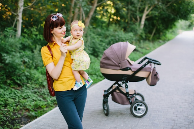 Een jonge roodharige vrouw in een geel shirt loopt met een kleine baby in een wandelwagen op een heldere zomerdag in het park