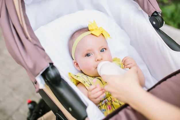 Een jonge roodharige vrouw in een geel shirt loopt met een kleine baby in een wandelwagen op een heldere zomerdag in het park