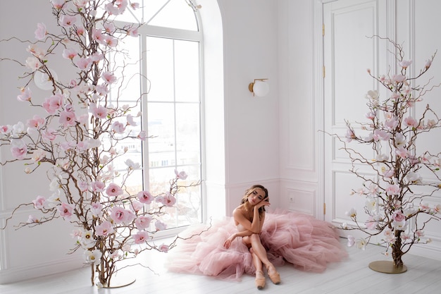 een jonge slanke ballerina danst in een lichte kamer bij het raam in een jurk