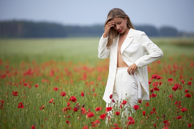 Foto een jonge slanke vrouw in een wit kostuum loopt in een bloemenveld met papaver in de zomer