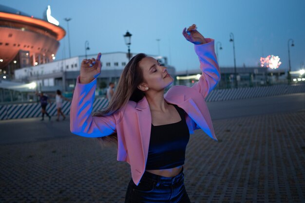Een jonge stijlvolle brunette in een roze jasje die blauw licht verlicht