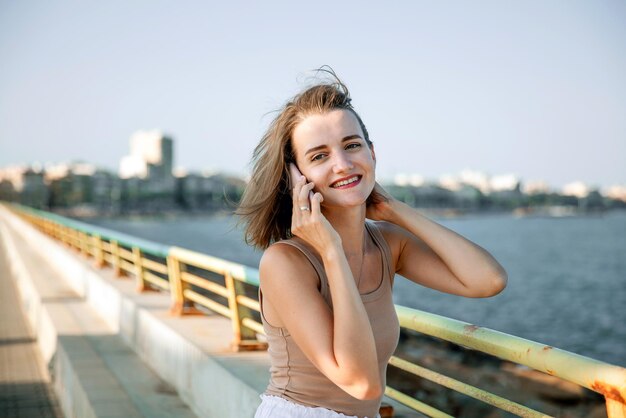 Een jonge stijlvolle vrouw communiceert op een smartphone tegen de achtergrond van een stadszeegezicht