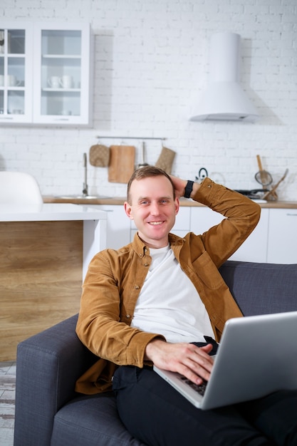 Een jonge succesvolle man zit thuis op de bank met een laptop en werkt. Werken op afstand tijdens quarantaine.