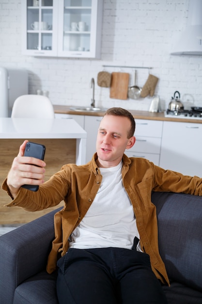 Een jonge succesvolle man zit thuis op de bank met een telefoon en praat via een videolink. Werken op afstand tijdens quarantaine.