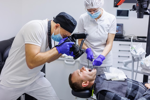 Foto een jonge tandarts maakt een foto van het gebit van de patiënt de assistent helpt de dokter tandartspraktijk