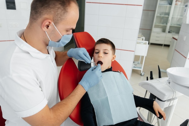 Een jonge tandarts onderzoekt en behandelt de tanden van een achtjarige jongen in moderne witte tandheelkunde close-up Tandprothese behandeling en tanden bleken Moderne tandheelkunde Preventie