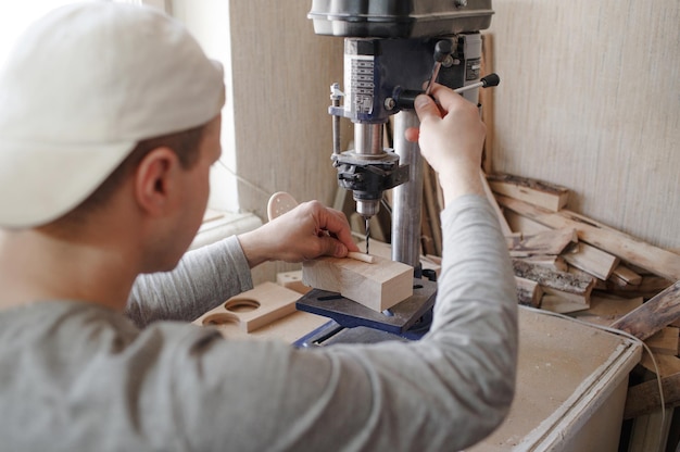 Een jonge timmerman gebruikt een boormachine om gaten in een houten plank te boren