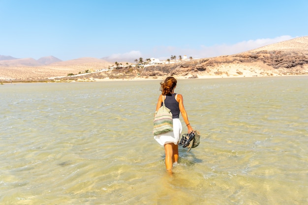 Een jonge toerist die op een herfstochtend door het kristalheldere water op het strand van Sotavento loopt in het zuiden van Fuerteventura, Canarische Eilanden. Spanje