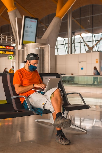 Een jonge toerist met een gezichtsmasker die zit te wachten om bijna lege luchthavens op te stijgen