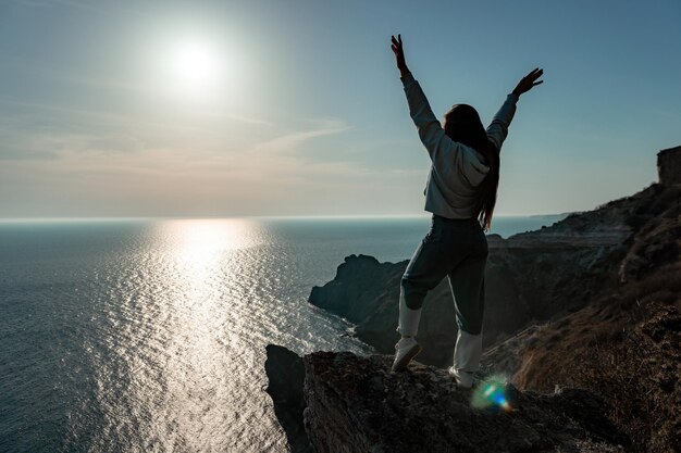 Een jonge toeristenvrouw die geniet van de zonsondergang boven het berglandschap van de zee terwijl ze buiten yoga voor vrouwen zit