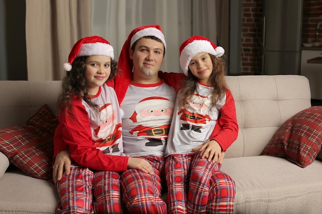 een jonge vader in kerstpyjama en een kerstmuts kust zijn dochtertjes