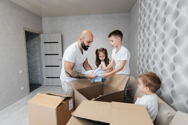 Een jonge vader met kinderen pakt een doos met dingen uit nadat hij naar een nieuw appartement is verhuisd Aankoop van onroerend goed Inwijdingsfeest levering en transport van goederen