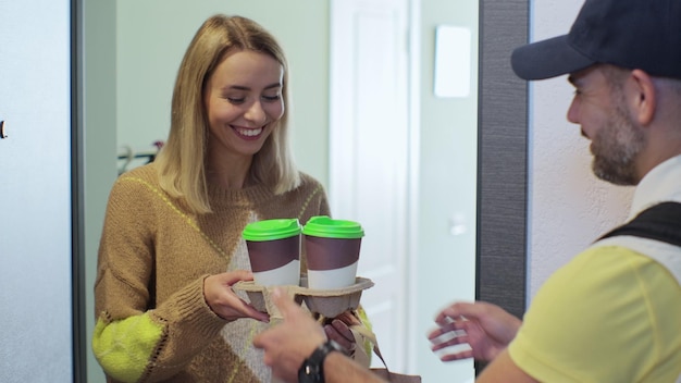 Een jonge voedselbezorger in een geel uniform Man die koffie en eten bezorgt aan een mooie vrouw thuis Binnen schot Voedselbezorgingsconcept