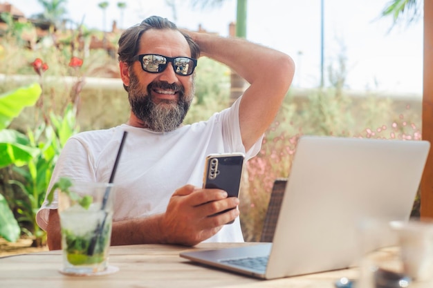 Een jonge volwassen man aan het werk buiten in het café mojito drinken Alternatieve levensstijl op kantoor en op het werk Moderne zakelijke online concept Een mannelijke mensen met laptopcomputer en telefoon hebben plezier bellen