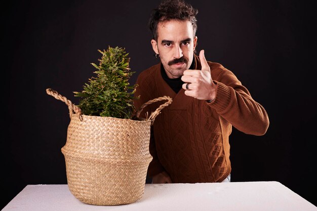 Een jonge volwassene geeft een duim omhoog naast een marihuana plant met zwarte achtergrond