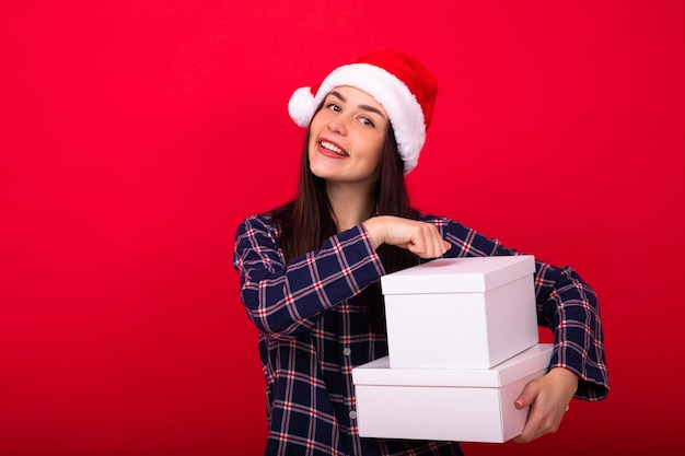 Een jonge vrolijke vrouw in feestelijke pyjama's houdt nieuwjaarsgeschenken op een rode achtergrond in de studio