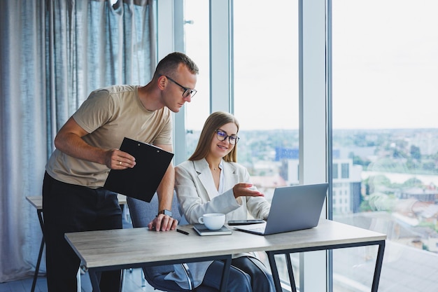 Een jonge vrouw aan een laptop met een bril zit aan een tafel met een zakelijke zakelijke bijeenkomst met collega's in een modern kantoor zakelijke carrièreconcept Vrije ruimte selectieve focus