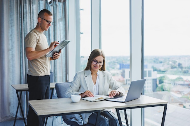 Een jonge vrouw aan een laptop met een bril zit aan een tafel met een zakelijke zakelijke bijeenkomst met collega's in een modern kantoor zakelijke carrièreconcept Vrije ruimte selectieve focus