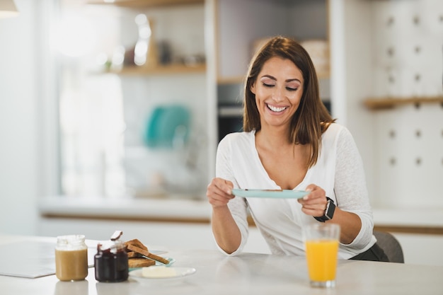 Een jonge vrouw aan het ontbijten en genieten van een zonnige ochtend in haar keuken.