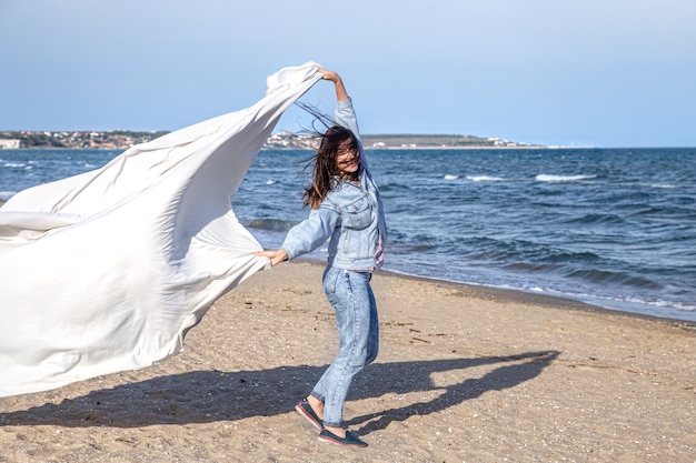 Een jonge vrouw aan zee heeft plezier met het vasthouden van een groot laken in de wind, een vrije levensstijl.