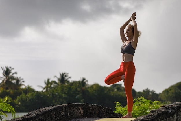 Een jonge vrouw beoefent yoga aan de oceaankust tijdens zonsopgang