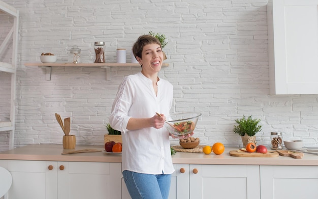 Een jonge vrouw bereidt een groentesalade in haar keuken Mengt groenten in een groot bord Het concept van een gezonde levensstijl