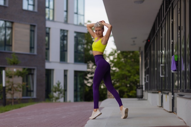 Een jonge vrouw bereidt zich voor op buitensporten op de moderne promenade in de buurt van haar appartementencomplex.