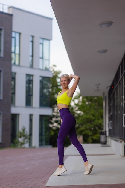 Een jonge vrouw bereidt zich voor op buitensporten op de moderne promenade in de buurt van haar appartementencomplex.