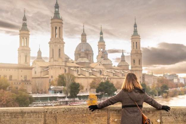 Een jonge vrouw bij zonsondergang op de stenen brug naast de Basilica De Nuestra SeÃÃ‚Â±ora del Pilar aan de rivier de Ebro in de stad Zaragoza, Aragon. Spanje