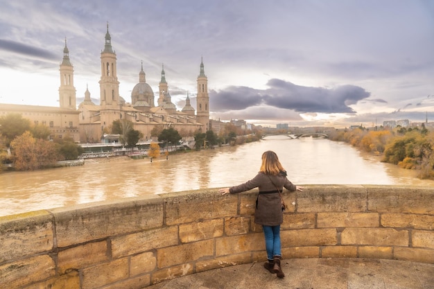 Een jonge vrouw bij zonsondergang op de stenen brug naast de Basilica De Nuestra SeÃÃ‚Â±ora del Pilar aan de rivier de Ebro in de stad Zaragoza, Aragon. Spanje