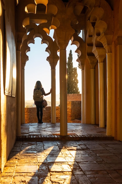 Een jonge vrouw bij zonsondergang vanaf de Arabische deuren van een binnenplaats van het Alcazaba in de stad Malaga, Andalusië. Spanje. Middeleeuws fort in Arabische stijl, verticale foto