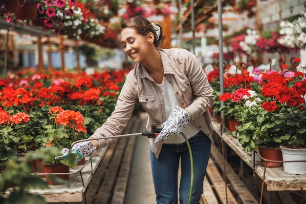 Een jonge vrouw die bloemen water geeft en ze verzorgt in een tuincentrum of plantenkwekerij.