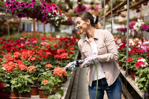 Een jonge vrouw die bloemen water geeft en ze verzorgt in een tuincentrum of plantenkwekerij.