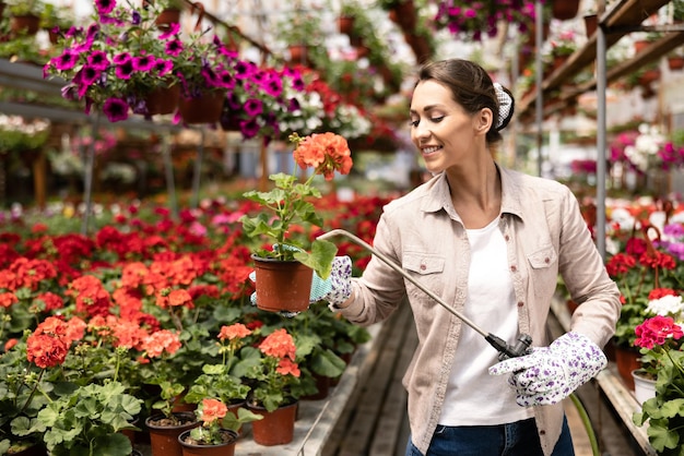 Een jonge vrouw die bloemen water geeft en ze verzorgt in een tuincentrum of plantenkwekerij.