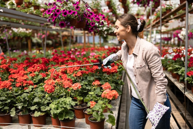 Een jonge vrouw die bloemen water geeft en ze verzorgt in een tuincentrum of plantenkwekerij.