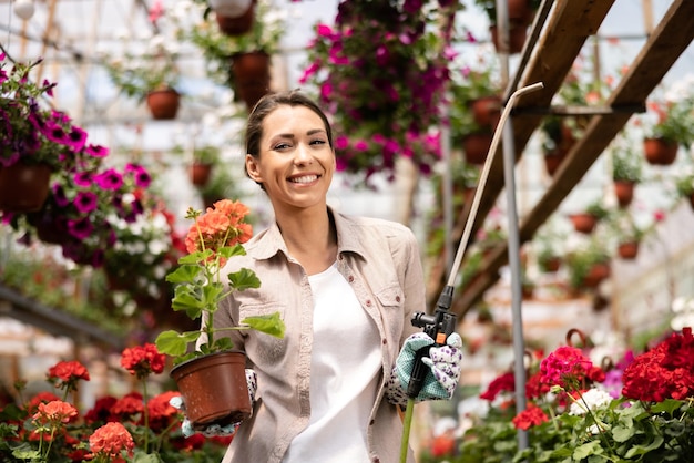 Een jonge vrouw die bloemen water geeft en ze verzorgt in een tuincentrum of plantenkwekerij.