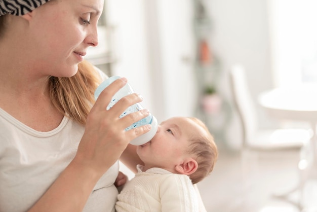 Een jonge vrouw die de pasgeboren baby voedt met babymelk, kunstmatige voeding, moeder39s liefde en warmte