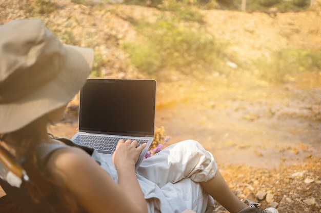 Een jonge vrouw die een berg beklimt en zit terwijl ze een computer of labtop gebruikt bij zonsondergang