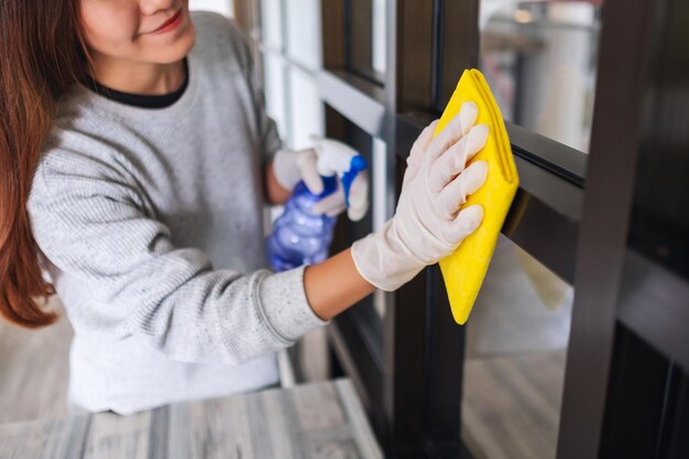 Een jonge vrouw die een beschermende handschoen draagt die het raam schoonmaakt voor huishoudelijk werkconcept